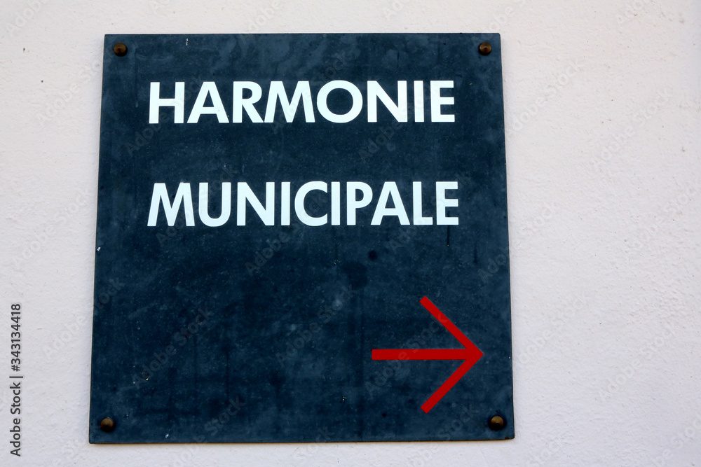 Panneau avec l'inscription Harmonie Municipale et une flèche rouge indiquant le sens de la salle de répétition de musique. Panneau avec l'inscription Harmonie Municipale et une flèche rouge indiquant le sens de la salle de répétition de musique.