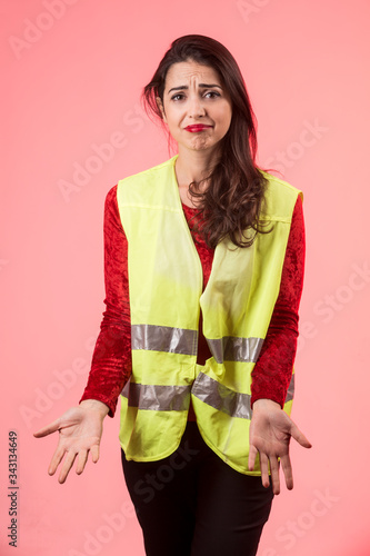 Ragazza mora che indossa una maglia rossa e un gilet giallo ad alta visibilità, è disperata e non sà cosa fare ,isolata su sfondo rosa photo