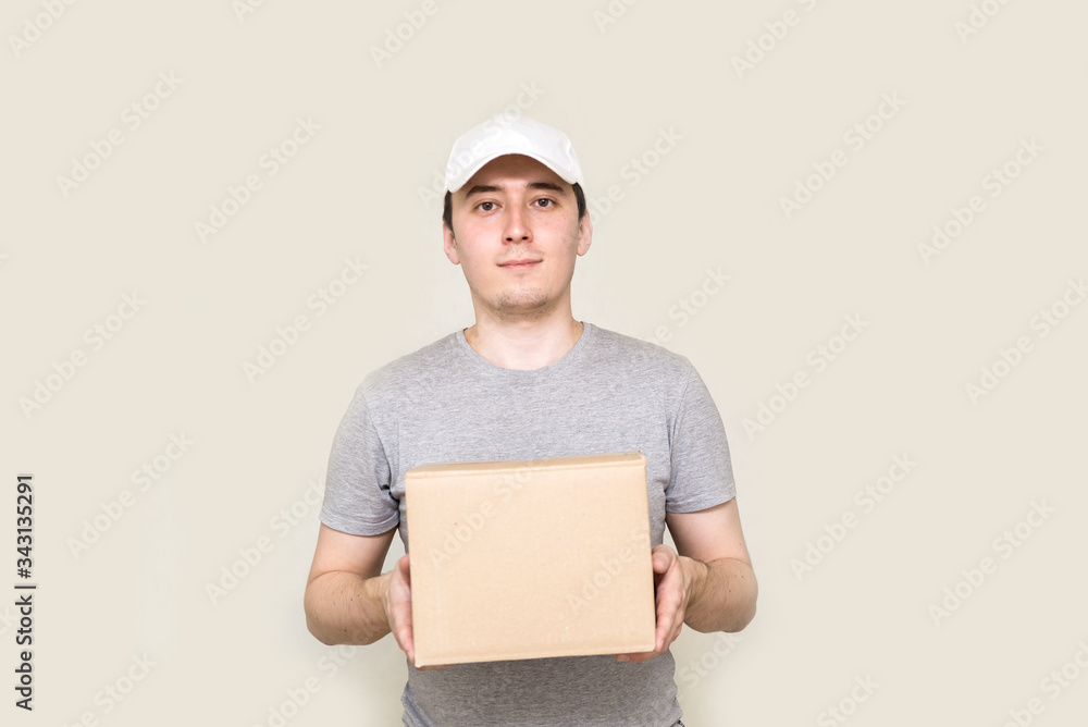 The courier is holding a cardboard box, the parcel on a gray background copy space. Fast delivery of the product by courier. Food delivery. Online stores and Express delivery . social distancing The courier is holding a cardboard box, the parcel on a gray background copy space. Fast delivery of the product by courier. Food delivery. Online stores and Express delivery . social distancing