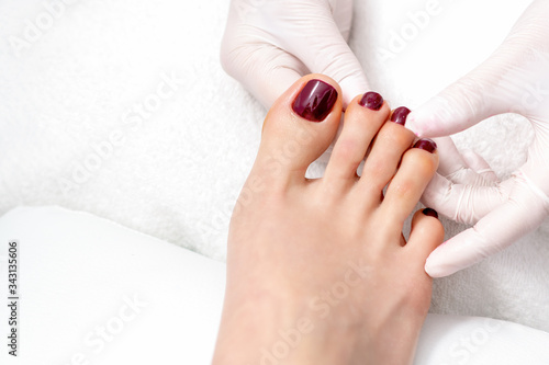 Pedicurist hands showing woman toenails painted in dark red color, top view.
