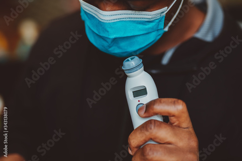 Fotografie African american man using a temporal thermometer to record his temperature by r
