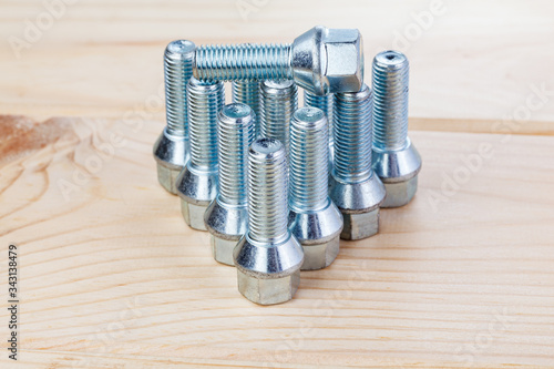 Automobile bolts. Metall bolts to fix the wheels of a car on a wood background in a photo studio. Spare consumables for replacing a wheel in a garage or workshop. Close-up.