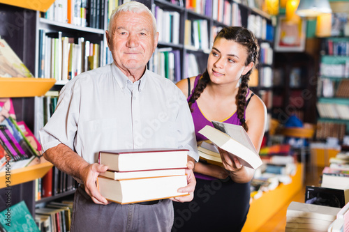 Old man with granddaughter are choosing books