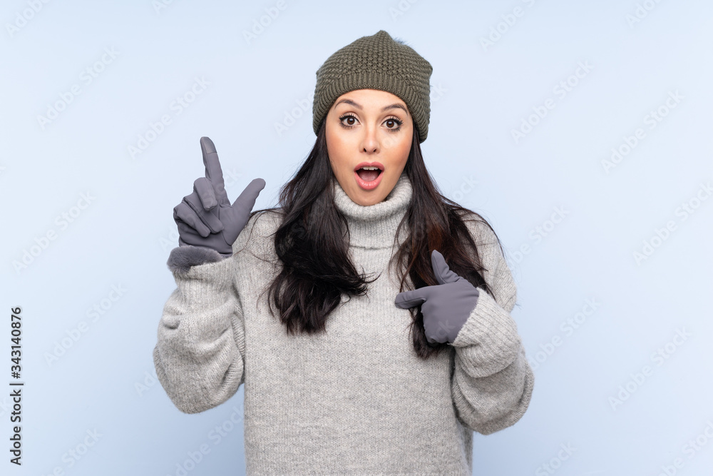 Young Colombian girl with winter hat over isolated blue background with surprise facial expression Young Colombian girl with winter hat over isolated blue background with surprise facial expression