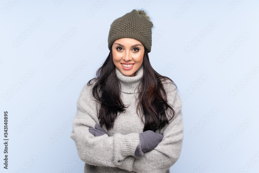 Young Colombian girl with winter hat over isolated blue background laughing Young Colombian girl with winter hat over isolated blue background laughing