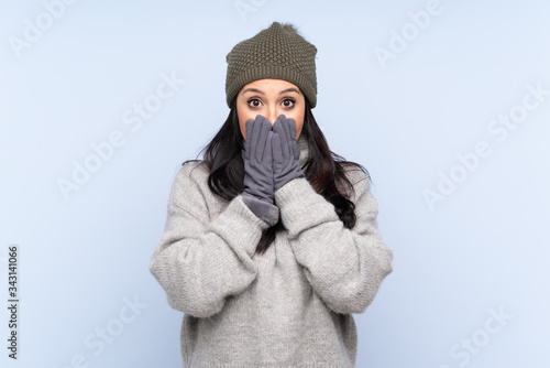 Young Colombian girl with winter hat over isolated blue background with surprise facial expression © luismolinero