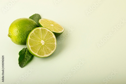 Fresh green limes on a pastel background. Mint leaves are laid out in the background and complement the composition. Whole fruits and halves lie on a wooden base. Fruit layout of lime and mint.