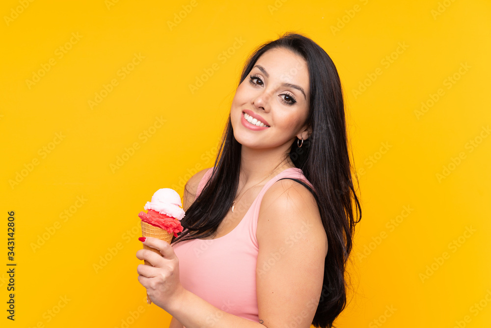 Young Colombian girl holding an cornet ice cream over isolated yellow background smiling a lot Young Colombian girl holding an cornet ice cream over isolated yellow background smiling a lot