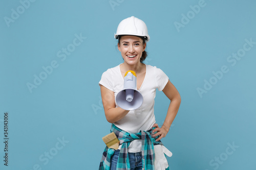 Cheerful young woman in casual clothes, protective helmet hardhat hold megaphone isolated on pastel blue background studio. Instruments accessories for renovation apartment room. Repair home concept. photo