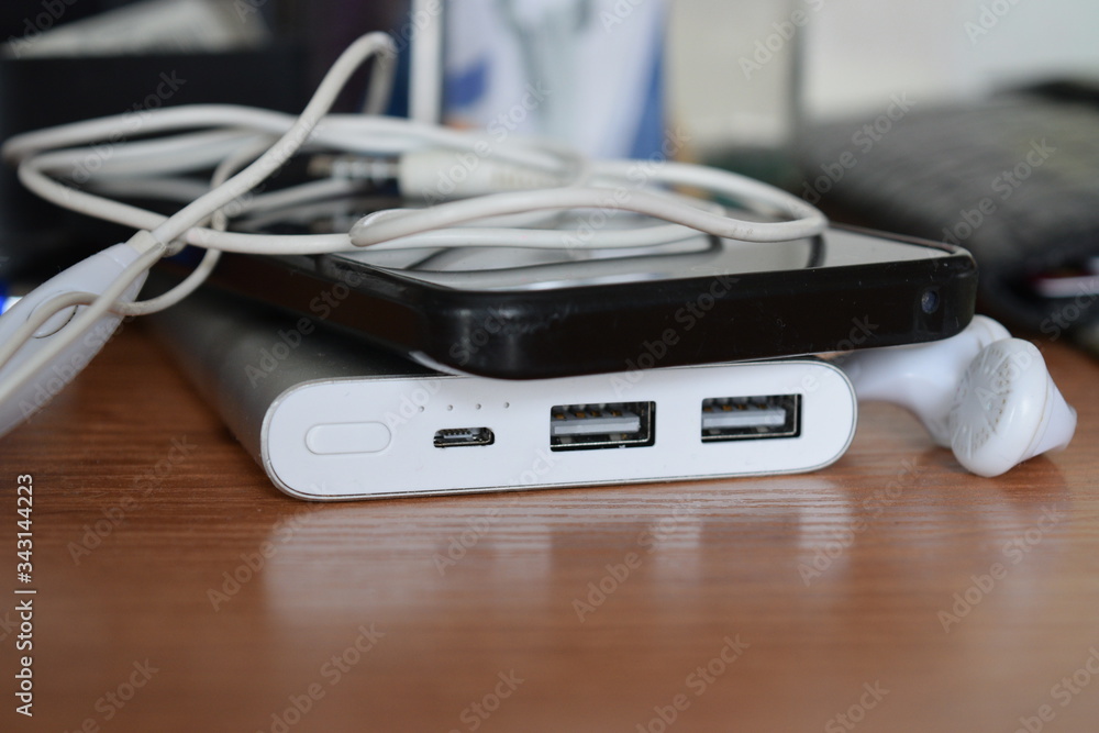 Silver power bank and a black phone are lying on the table Silver power bank and a black phone are lying on the table