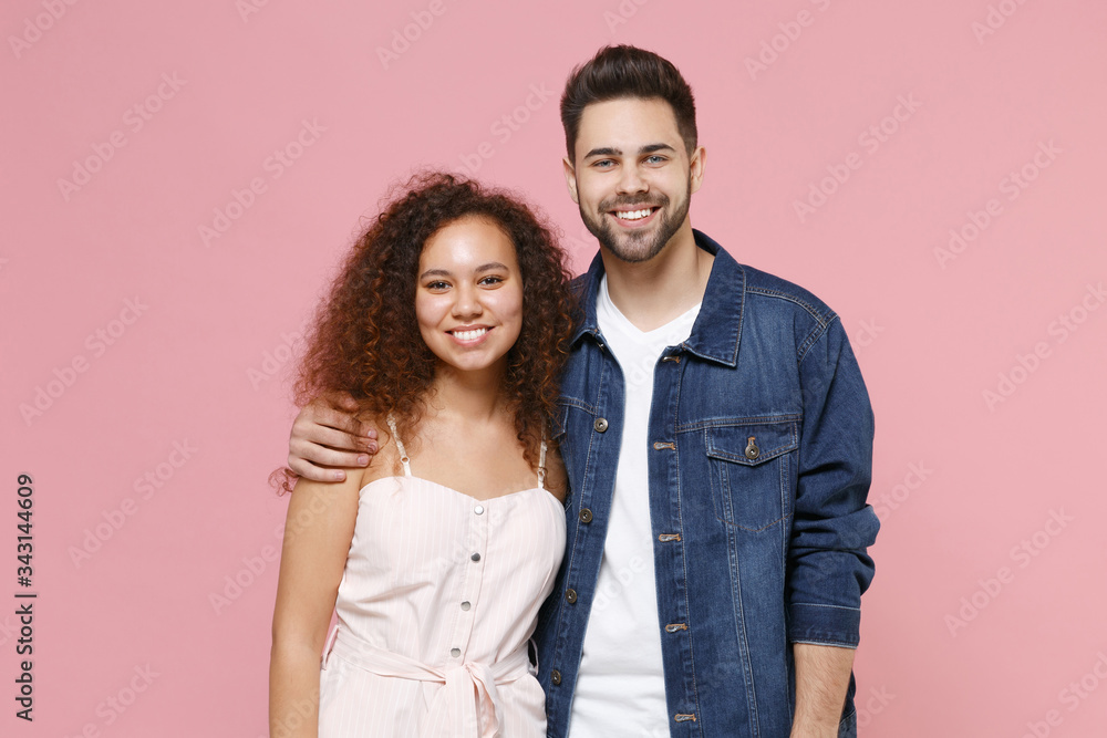Smiling young couple two friends european guy african american girl in casual clothes posing isolated on pastel pink background. People lifestyle concept. Mock up copy space. Hugging, looking camera. Smiling young couple two friends european guy african american girl in casual clothes posing isolated on pastel pink background. People lifestyle concept. Mock up copy space. Hugging, looking camera.