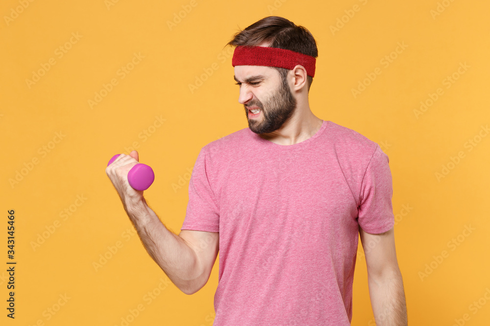 Naklejka premium Tired young bearded fitness sporty guy sportsman in headband t-shirt spend weekend in home gym isolated on yellow background. Workout sport motivation concept. Doing exercise for arms with dumbbell.