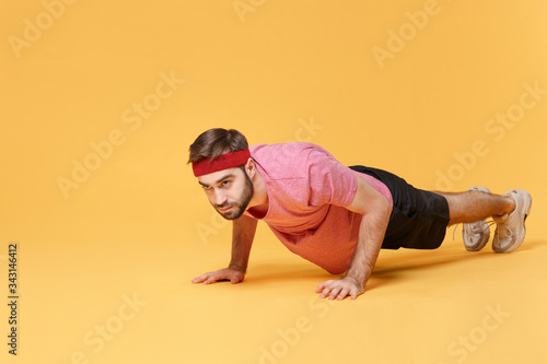 Young bearded fitness sporty guy sportsman in headband t-shirt spend weekend in home gym isolated on yellow background. Workout sport motivation lifestyle concept. Doing push-ups exercises on floor.