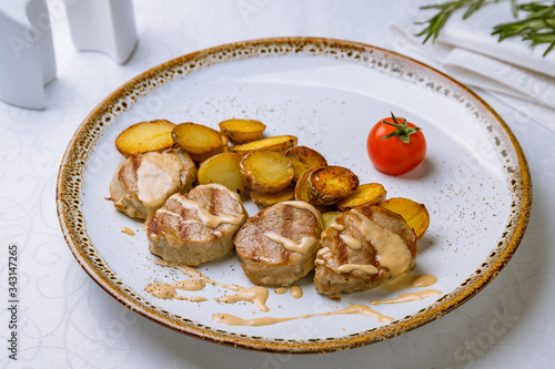 Pork medallions with baked mini potatoes on white plate