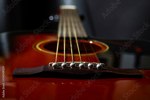 Guitar String holder and lower threshold of a six-string acoustic guitar close-up on a black background.