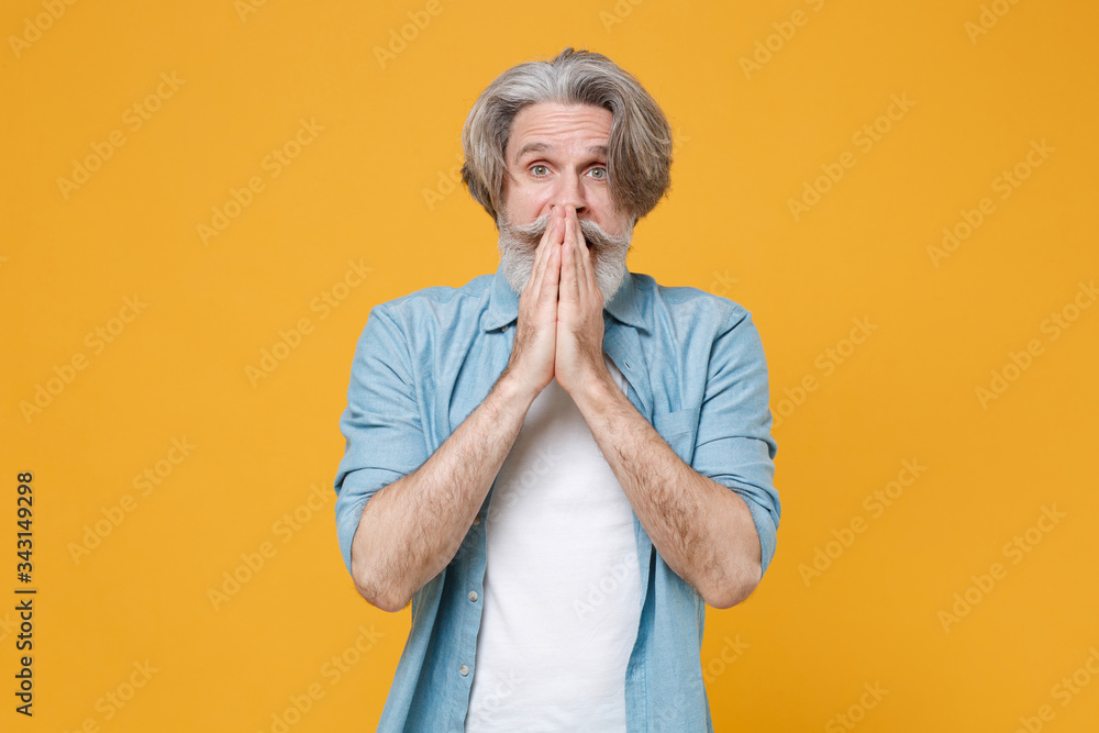 Shocked elderly gray-haired mustache bearded man in casual blue shirt posing isolated on yellow background studio portrait. People lifestyle concept. Mock up copy space. Covering mouth with hands. Shocked elderly gray-haired mustache bearded man in casual blue shirt posing isolated on yellow background studio portrait. People lifestyle concept. Mock up copy space. Covering mouth with hands.