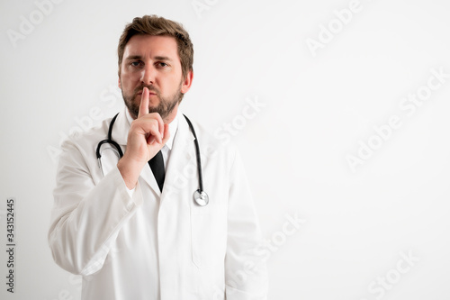 Male doctor with stethoscope in medical uniform showing shh gesture