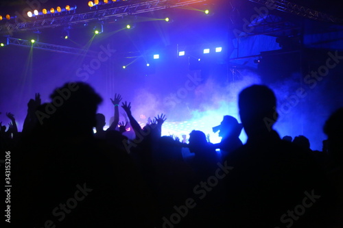 Picture of rock concert, music festival, New Year eve celebration, party in nightclub, dance floor, disco club, many people standing with raised hands up and clapping, happiness and night life concept © Subin Sailendran 