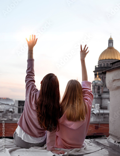 Two girls are sitting back view on the roof