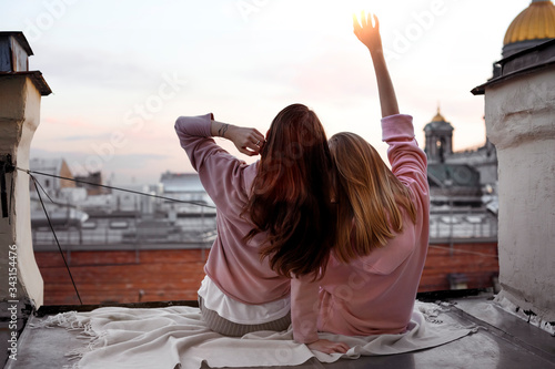 Two girls are sitting back view on the roof