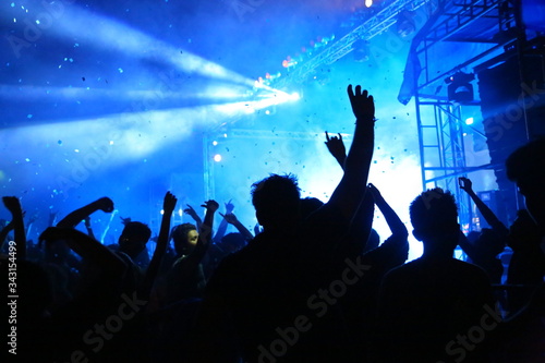Picture of rock concert, music festival, New Year eve celebration, party in nightclub, dance floor, disco club, many people standing with raised hands up and clapping, happiness and night life concept