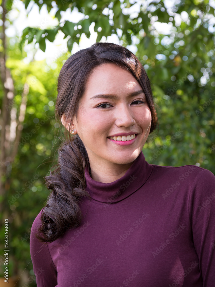 Portrait of a young Asian woman smiling while standing in park with bokeh; Woman's face with make-up and hairstyle Portrait of a young Asian woman smiling while standing in park with bokeh; Woman's face with make-up and hairstyle