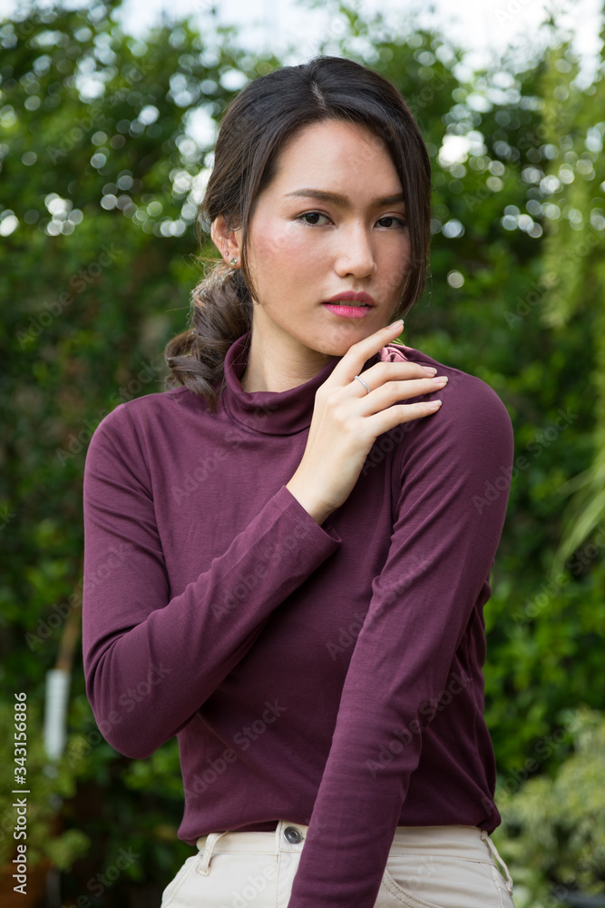 Portrait of a young Asian woman smiling while standing in park with bokeh; Woman's face with make-up and hairstyle Portrait of a young Asian woman smiling while standing in park with bokeh; Woman's face with make-up and hairstyle