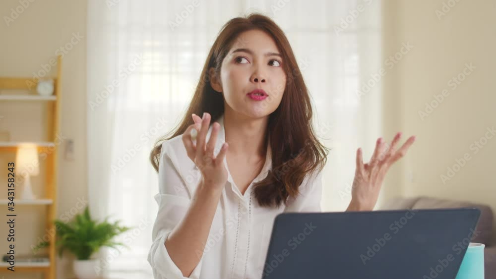 Asian businesswoman using laptop talk to colleagues about plan in video call while smart working from home at living room. Self-isolation, social distancing, quarantine for coronavirus prevention. Asian businesswoman using laptop talk to colleagues about plan in video call while smart working from home at living room. Self-isolation, social distancing, quarantine for coronavirus prevention.