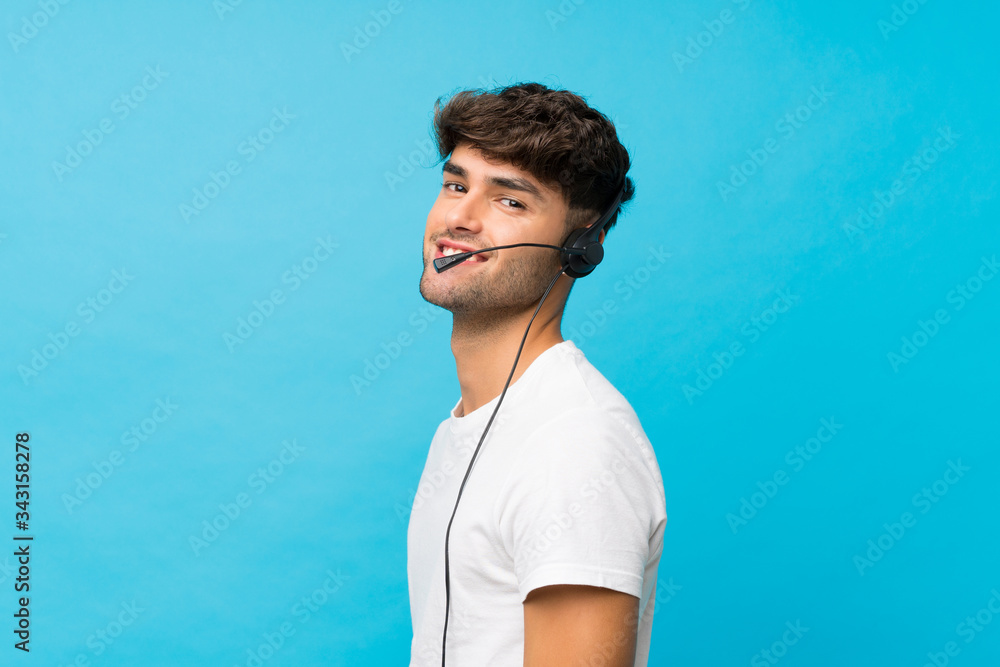 Young handsome man over isolated blue background working with headset Young handsome man over isolated blue background working with headset