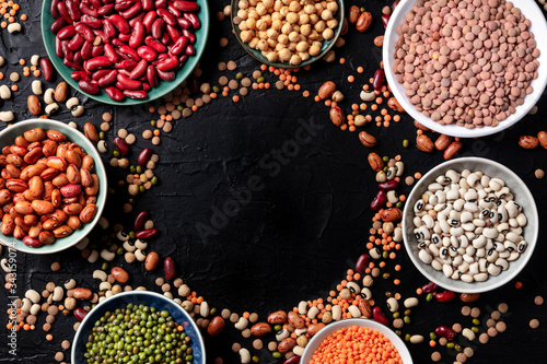 Legumes assortment, shot from the top on a black background with a place for text. Lentils, soybeans, chickpeas, red kidney beans, a vatiety of pulses, forming a frame
