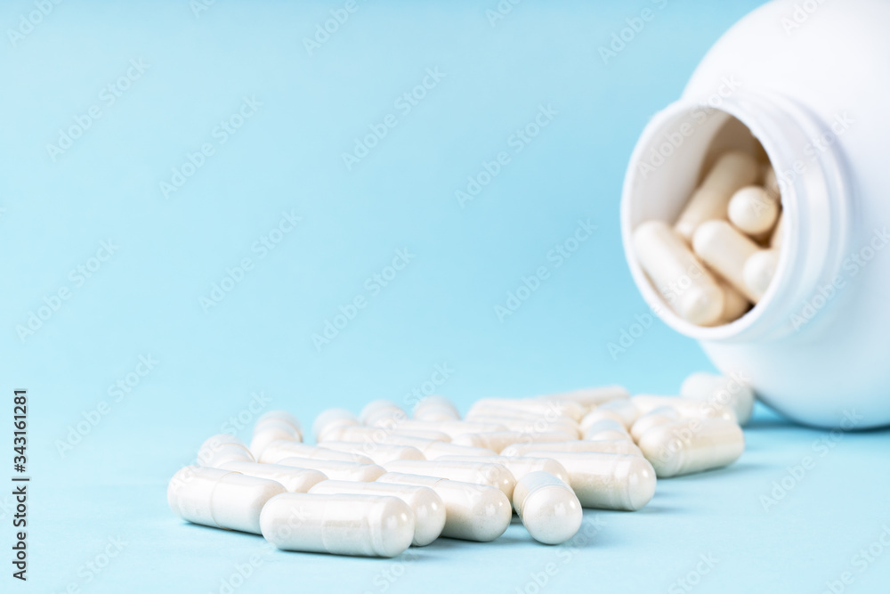 White medical pills and capsules spilling out of bottle. Medication in white container on blue background. Healthcare, health insurance, medicine concept. Copy space, front view White medical pills and capsules spilling out of bottle. Medication in white container on blue background. Healthcare, health insurance, medicine concept. Copy space, front view