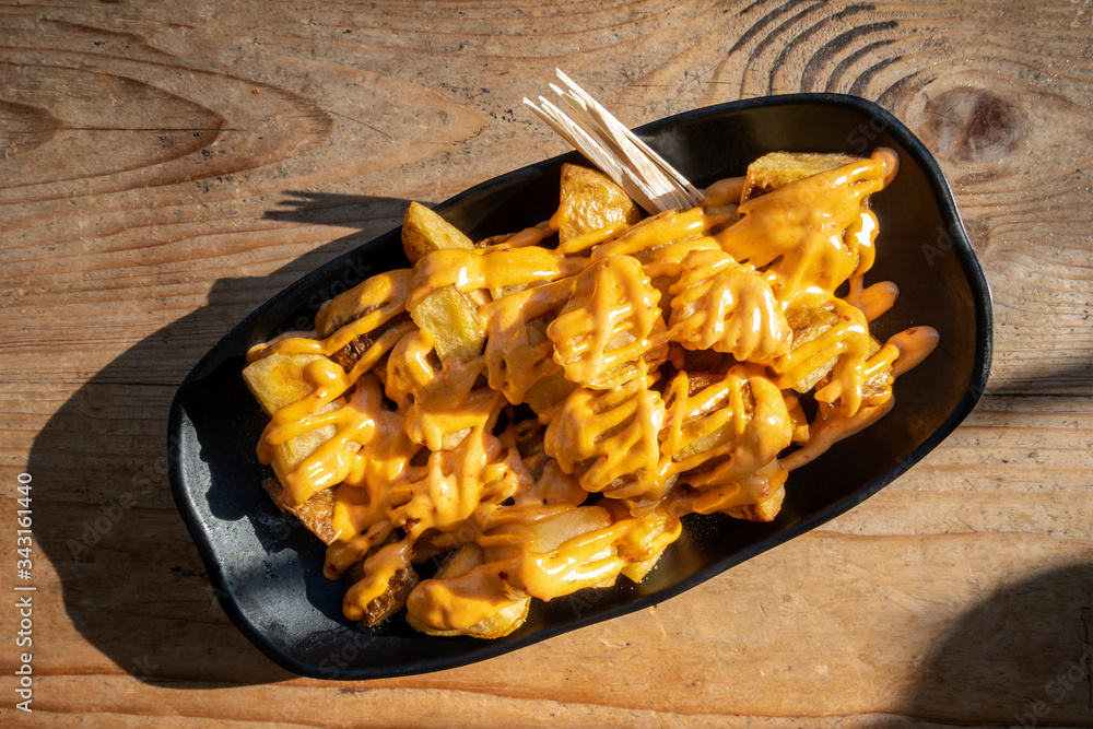 Patatas bravas, typical Spanish food. Potatos with a spicy sauce, shot from above on a wooden table Patatas bravas, typical Spanish food. Potatos with a spicy sauce, shot from above on a wooden table