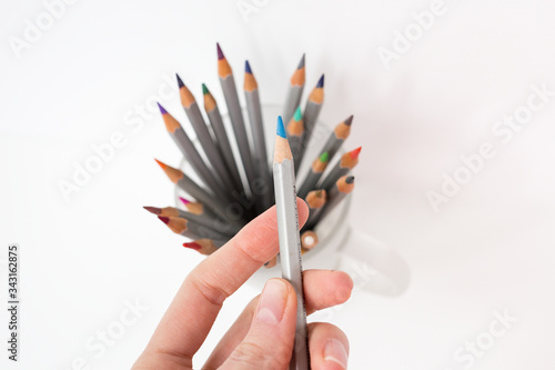 One green pensil on the hand. A colorful pencils in a glass in the white background. Drawing by pencils. Hobby during quarantine.  photo