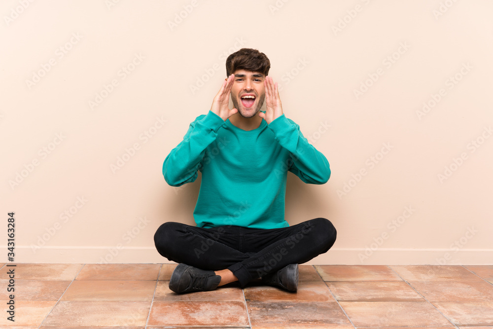 Young handsome man sitting on the floor shouting with mouth wide open