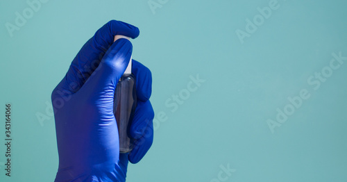 A hand in a rubber medical glove sprays anaesthetic on a green background.