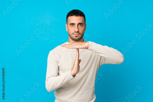 Young man over isolated blue background making time out gesture