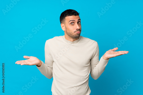 Young man over isolated blue background making doubts gesture