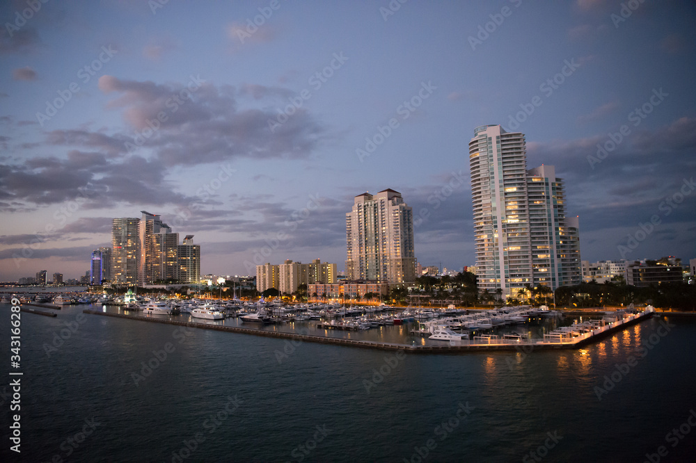 Fototapeta Urban paradise. City skyline. City and yacht club from sea. City architecture at dusk. Twilight of city. Illuminating lights on cloudy evening sky. Travelling and wanderlust. Travel destination