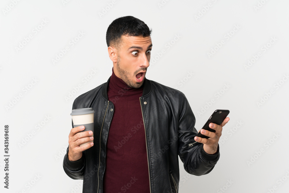 Young man over isolated white background holding coffee to take away and a mobile Young man over isolated white background holding coffee to take away and a mobile