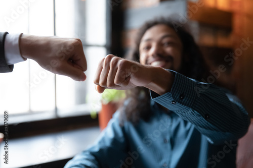 Fotografie Close up of happy diverse male friends greeting give fists bump meeting for drin