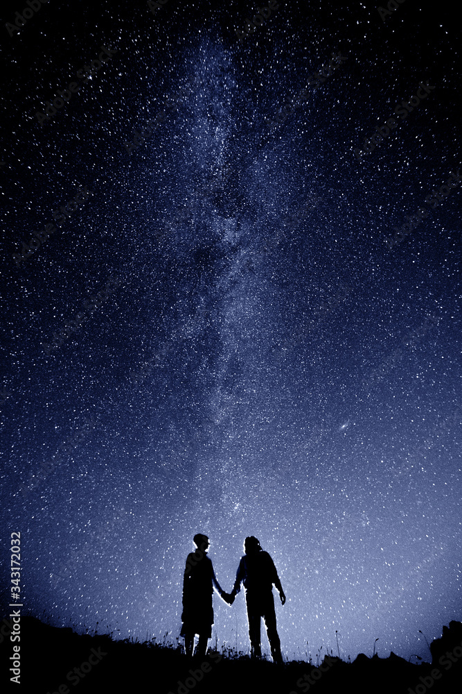 Couple is standing in mountains against night sky with milky way