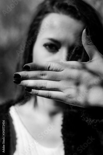 Young woman hiding her mouth with one hand. No freedom of speech, silence. Focus on the hand, black and white.