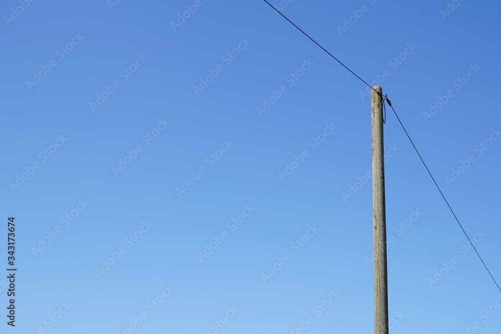 A single high voltage power line against blue cloudless sky. Overhead line on a wood pylon.