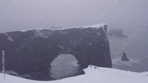 Dyrhólaey is a small peninsula with striking views, a lighthouse and a large arch of volcanic rock at sea during the cold Icelandic ridicule. Snowfall.