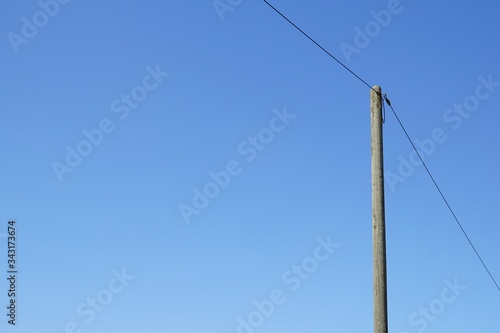 A single high voltage power line against blue cloudless sky. Overhead line on a wood pylon.