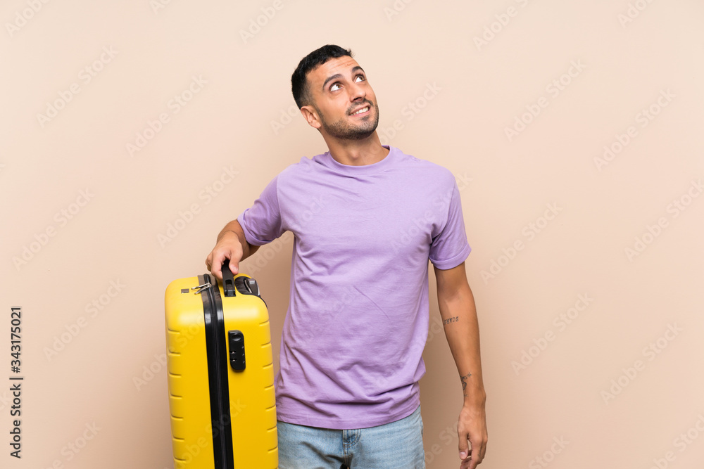 Man holding a suitcase over isolated background looking up while smiling