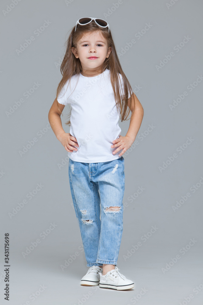 Kid girl preschooler in blue jeans, white t-shirt and sunglasses is posing  isolated on grey background Stock Photo | Adobe Stock