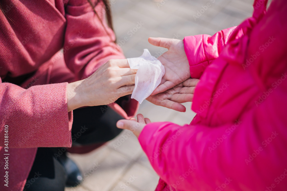Mom and daughter walk in the park during quarantine of the coronavirus. Mom rubs her daughter's hands with a napkin. Personal hygiene during the COVID-19 Pandemic