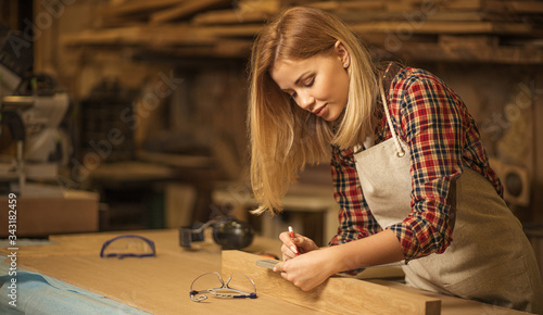 portrait of beautiful caucasian woman carpenter dealing with handicraft, woman has own business connected with making wooden furniture in workshop
