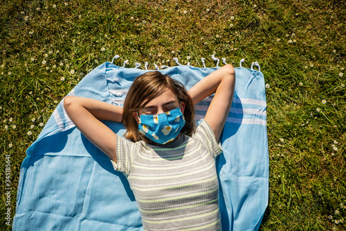 Eine Teenagerin mit selbstgenähten Mundschutz beim Sonnenbad in einem Park photo